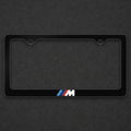 Black M Sport plate frame with blue and red stripes on a charcoal textured background
